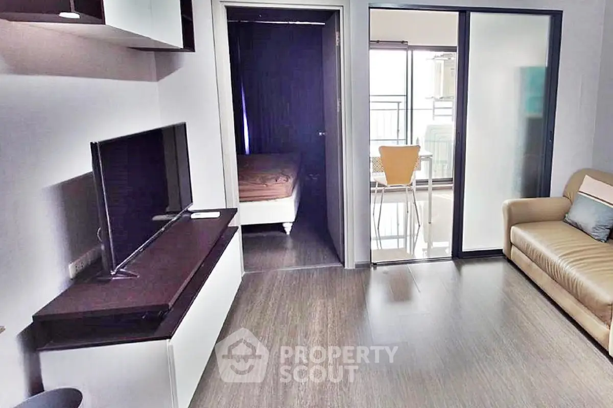 Modern living room with sleek TV setup and sliding glass doors leading to a cozy balcony.
