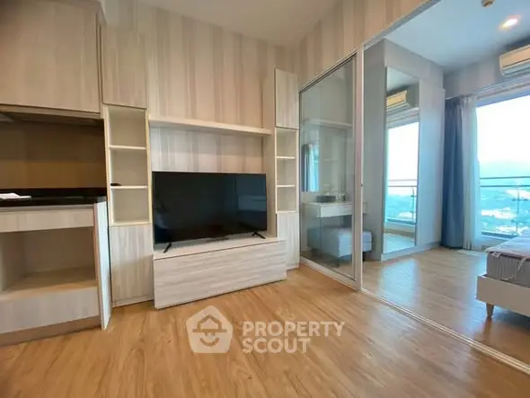 Modern living room with wooden flooring and large TV, adjacent to a balcony with scenic view.