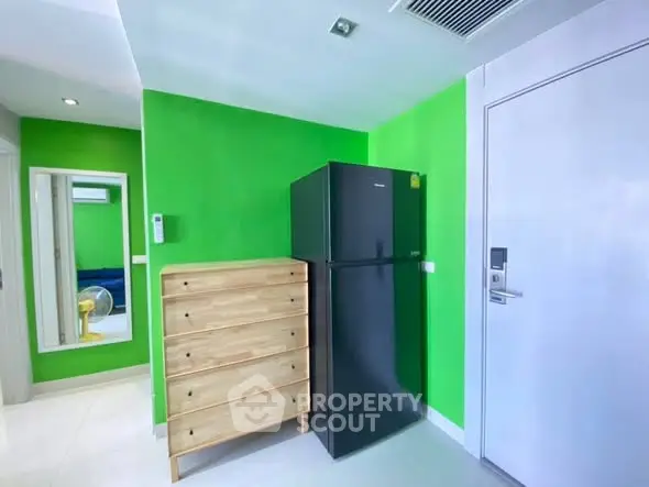 Modern apartment interior with vibrant green walls and sleek black refrigerator.