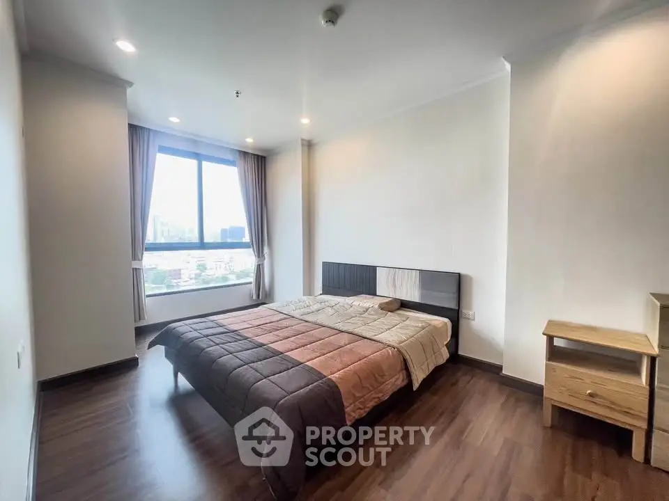 Spacious bedroom with city view and modern furnishings in a high-rise apartment.