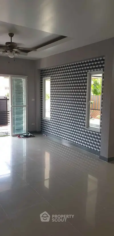 Spacious living room with modern geometric accent wall and ceiling fan, featuring large windows for natural light.