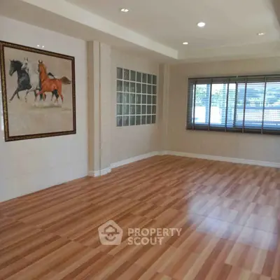 Spacious empty room with wooden flooring and large window, perfect for customization.