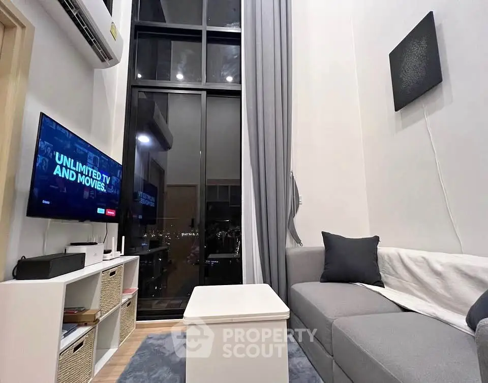 Modern living room with high ceiling and large window, featuring a cozy sofa and entertainment setup.