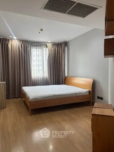 Spacious bedroom with wooden flooring and modern furnishings in a bright apartment.