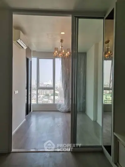 Modern apartment with large windows and city view, featuring a chandelier and sliding glass doors.