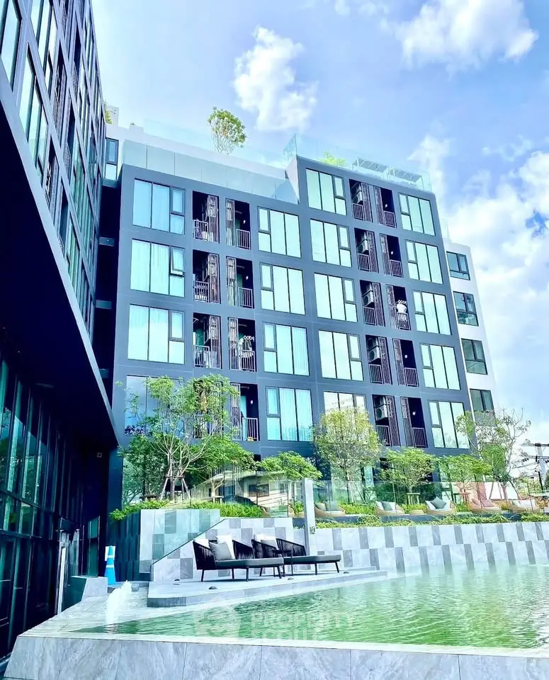 Modern apartment building with pool and lush greenery under a clear blue sky.
