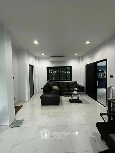 Spacious modern living room with sleek black furniture and elegant white tile flooring.