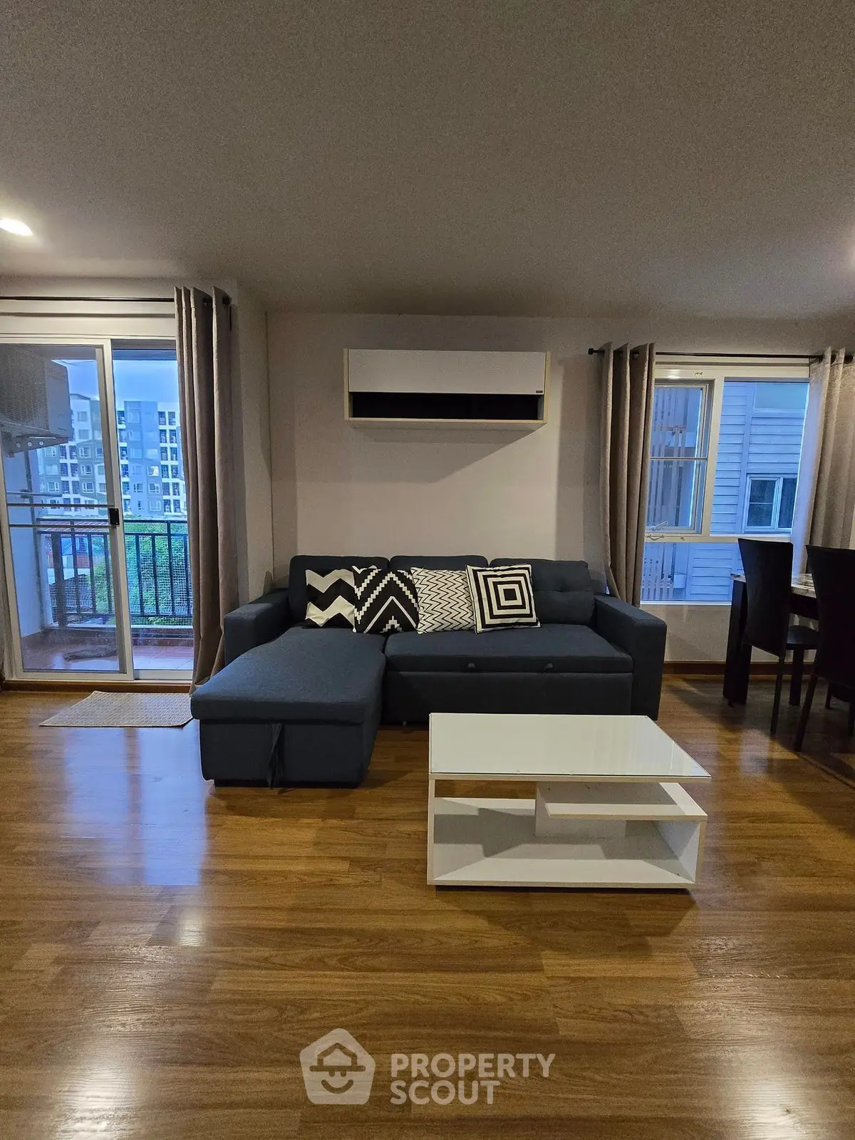Modern living room with stylish sofa and coffee table, featuring large windows and balcony access.