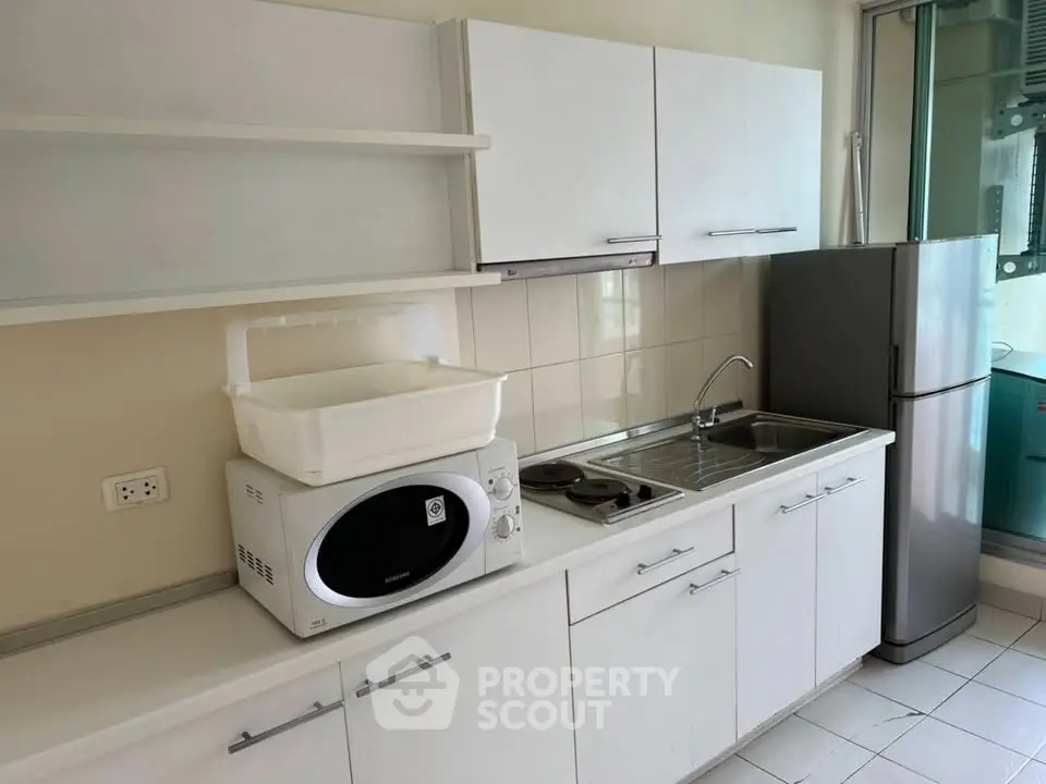 Modern kitchen with sleek white cabinets, stainless steel fridge, and microwave in a compact layout.