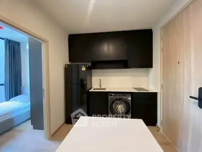 Modern compact kitchen with washing machine and sleek black cabinetry in a cozy apartment.