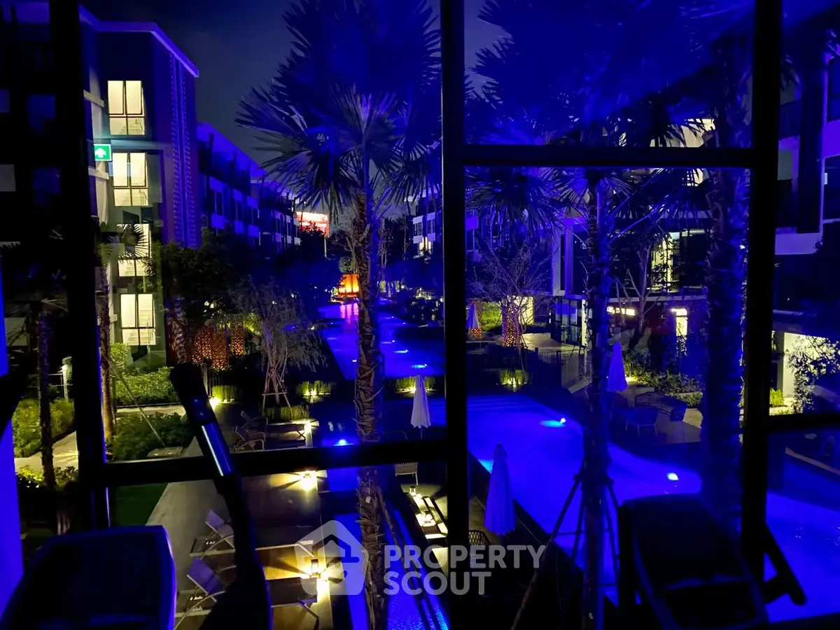 Stunning night view of a modern apartment complex with illuminated pool and lush landscaping.