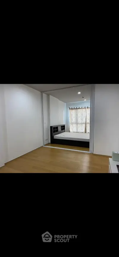 Spacious bedroom with wooden flooring and large window for natural light.