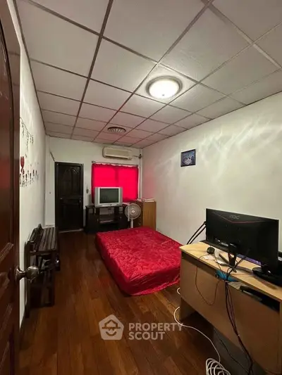 Cozy bedroom with wooden flooring, red accents, and a compact workspace setup.