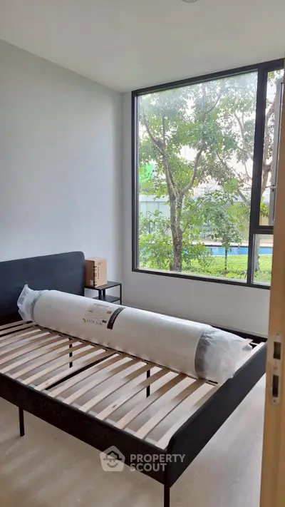 Spacious bedroom with large window and bed frame, offering serene garden view.