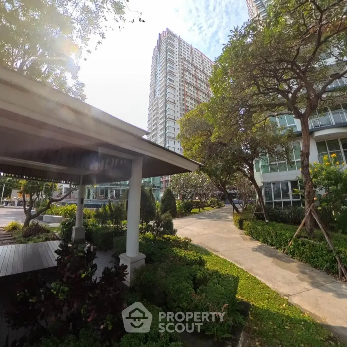 Lush garden view with modern high-rise building and shaded pavilion