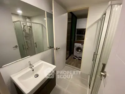 Modern bathroom with glass shower and washing machine in adjacent area.