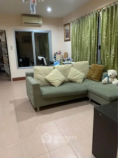 Cozy living room with green sofa and curtains, featuring air conditioning and tiled flooring.