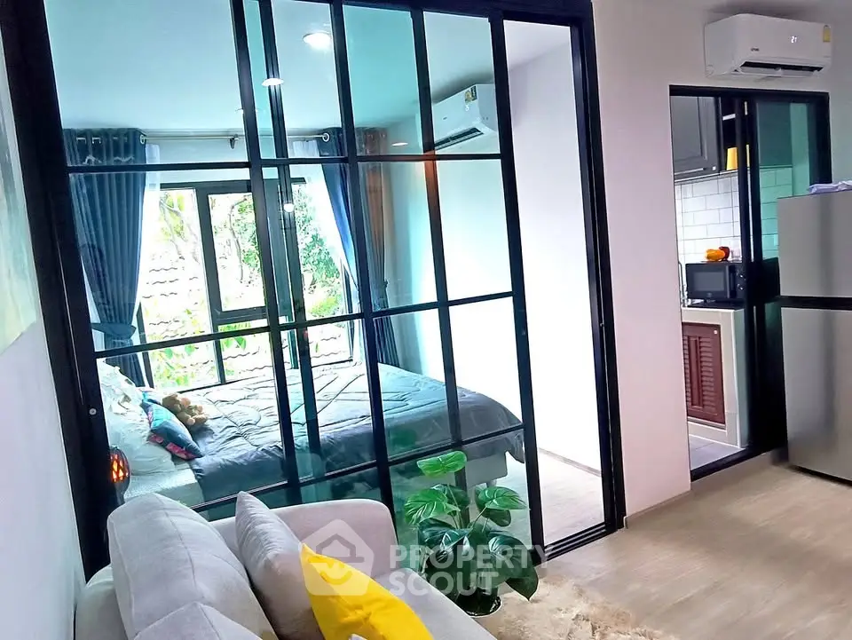 Modern apartment with glass-walled bedroom and cozy living area, featuring a compact kitchen and stylish decor.