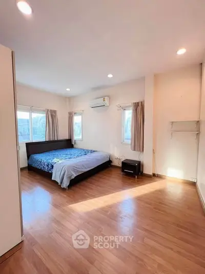Spacious bedroom with wooden flooring and natural light