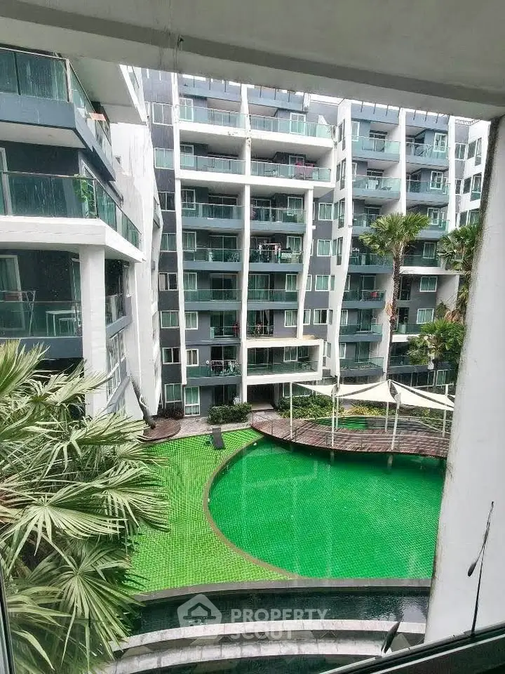 Modern apartment complex with a vibrant green pool and lush palm trees.