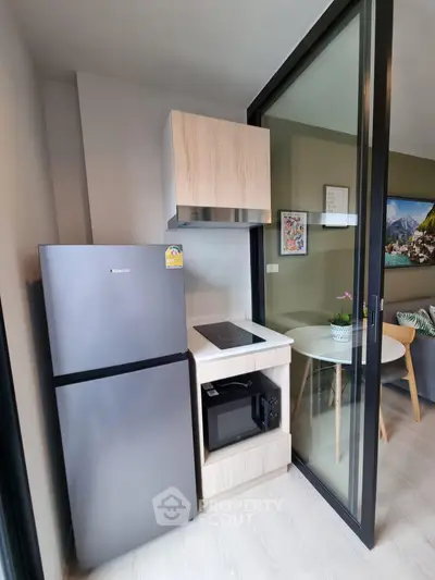 Modern compact kitchen with fridge, microwave, and induction cooktop in stylish apartment.