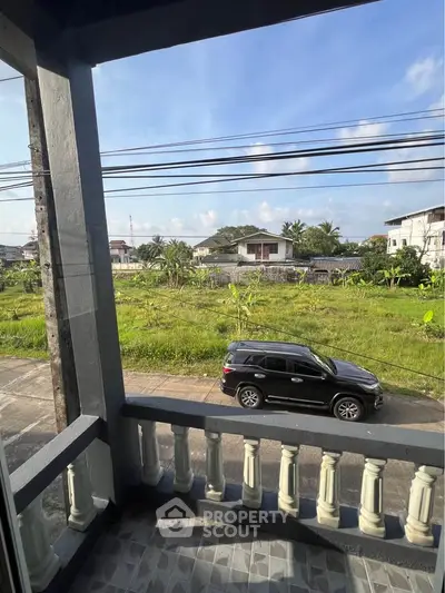 Charming balcony view overlooking lush greenery and suburban street, perfect for relaxation.