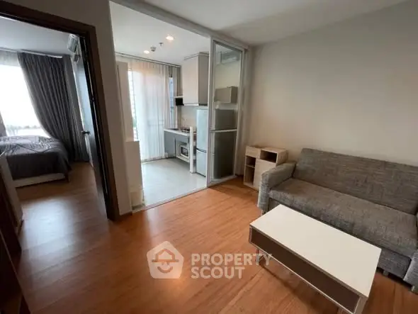 Modern apartment with open layout connecting living room and kitchen, featuring sleek furniture and natural light.