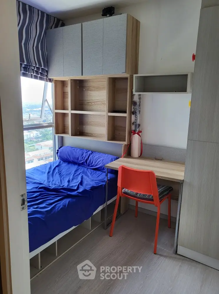 Cozy bedroom with built-in storage and study desk, featuring a vibrant city view.