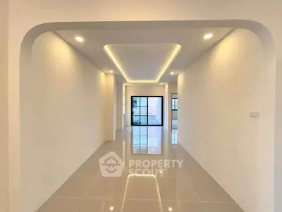 Spacious modern hallway with sleek lighting and glossy tiled floors leading to a bright room.