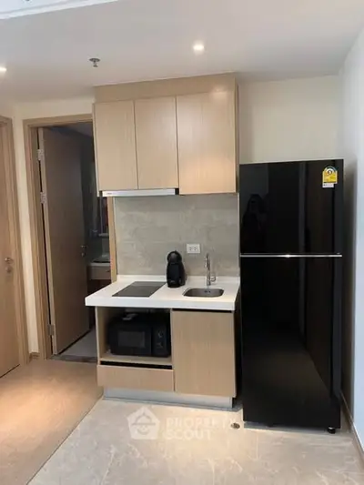 Modern compact kitchen with sleek black fridge and built-in appliances in a stylish apartment.
