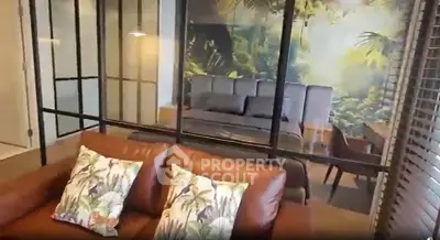 Stylish living room with leather sofa and glass partition leading to a cozy bedroom with nature-themed decor.