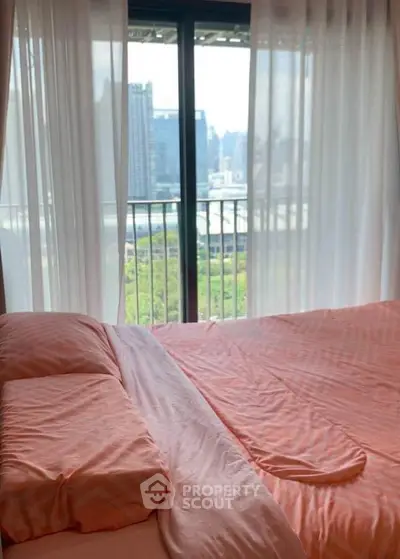 Cozy bedroom with city view and large windows, featuring soft pink bedding.