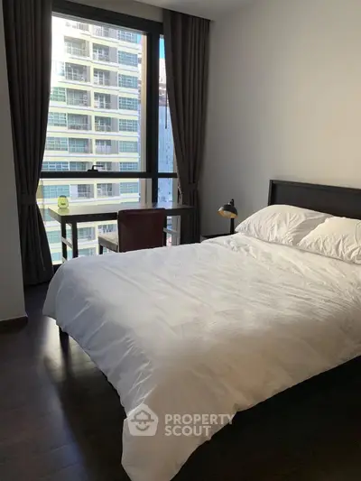 Modern bedroom with large window and city view, featuring a cozy bed and study desk.
