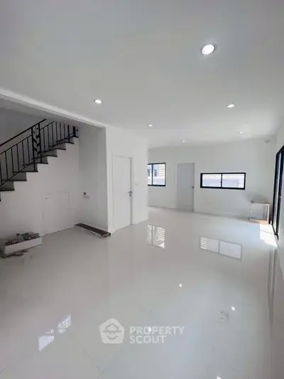 Spacious modern living room with glossy white tiles and staircase, ample natural light.