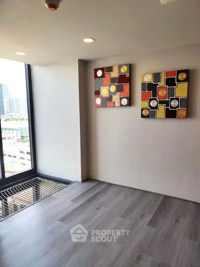 Modern apartment interior with large window and abstract wall art, offering city views and stylish flooring.