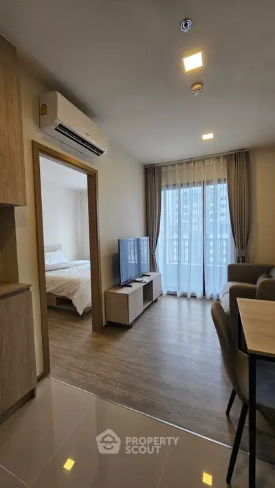 Modern apartment interior with open living room and bedroom, featuring sleek furniture and large windows.