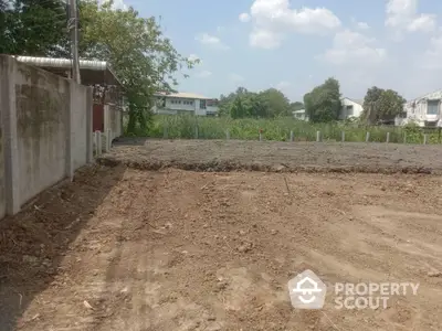 Spacious vacant lot ready for development, surrounded by a concrete wall and lush greenery, in a serene neighborhood.