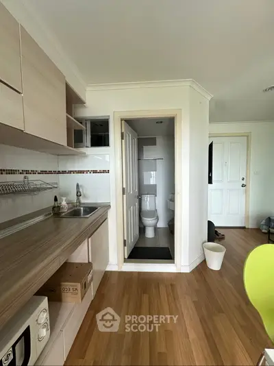 Modern compact kitchen with wooden cabinets and adjacent bathroom in cozy apartment.