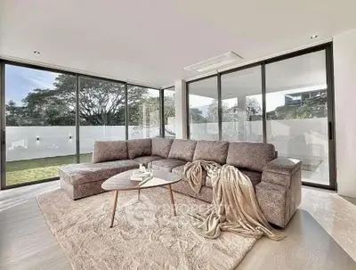 Luxurious modern living room with large windows and garden view, featuring a stylish sectional sofa and elegant decor.