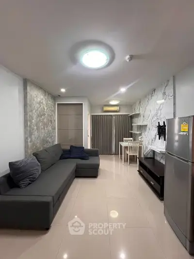 Modern living room with sleek gray sofa, marble accent wall, and dining area in open layout apartment.