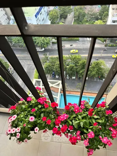 Charming balcony view with vibrant flowers overlooking city street and pool.