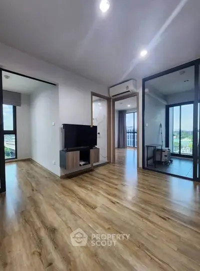 Spacious modern living room with wooden flooring and large windows offering natural light.