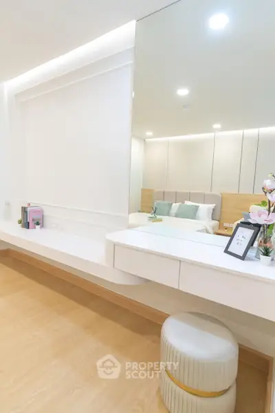 Elegant bedroom with modern vanity and plush stool, featuring soft lighting and stylish decor.
