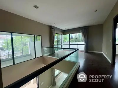 Spacious upper-level living area with gleaming hardwood floors, abundant natural light, and elegant glass balustrades offering an open, airy feel.