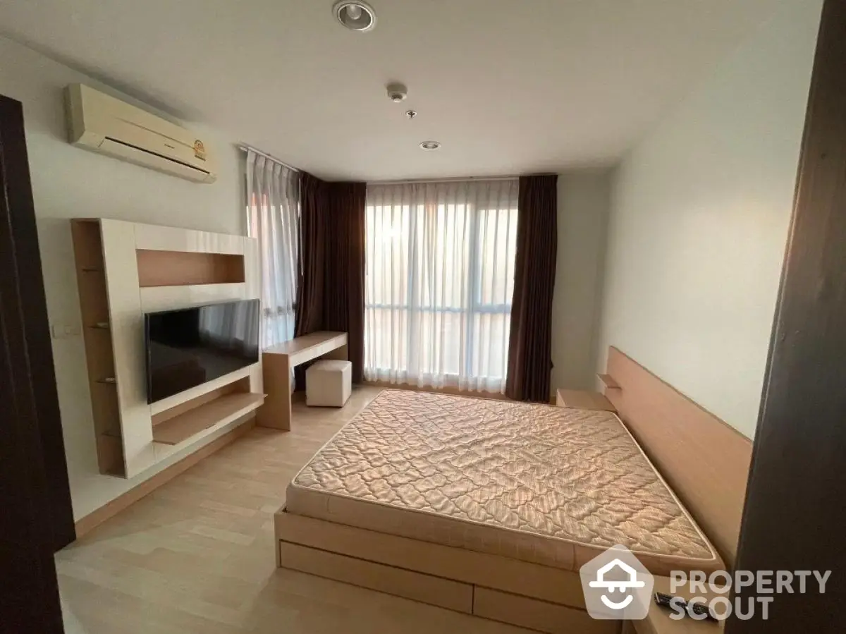 Modern bedroom with natural light and minimalist design featuring a built-in TV unit and air conditioning.