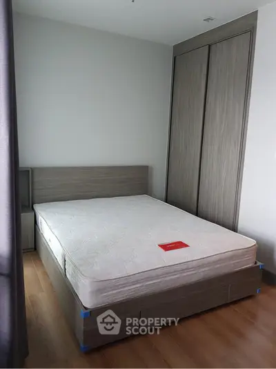 Modern bedroom with wooden flooring and built-in wardrobe, featuring a minimalist design and natural light.