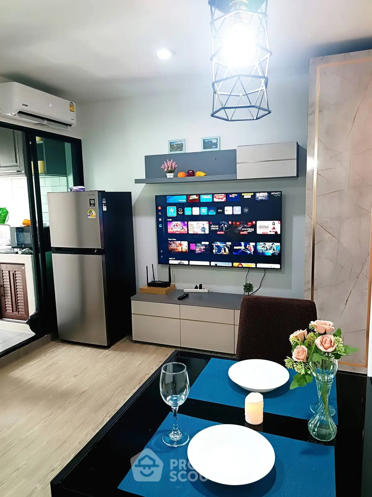 Modern living room with smart TV, dining setup, and sleek kitchen appliances in a cozy apartment.