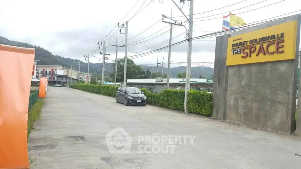 Entrance to commercial property with signage and parking area, surrounded by lush greenery and mountain views.