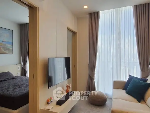 Modern living room with TV and adjacent bedroom, featuring elegant curtains and cozy seating.