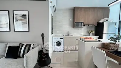 Modern open-plan living room and kitchen with stylish decor and appliances, including a washing machine and guitar.